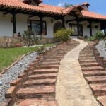Fachada este de casona tradicional colonial en Villa de Leyva con columnas de madera negras. Camino en adoquín y piedra.
